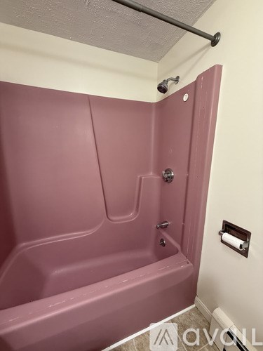 A pink bathtub in a bathroom with a towel rack on the wall.
