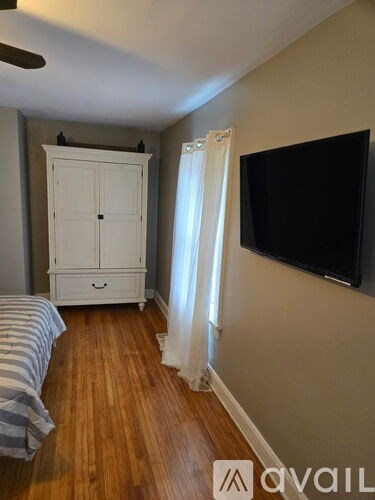 A bedroom with a bed, a dresser, a TV and a window with curtains.