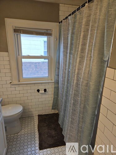 A bathroom with a toilet, a window, and a shower curtain.