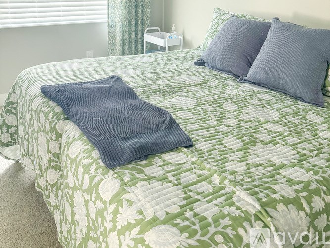 A bed with a green and white floral patterned comforter and two blue pillows.