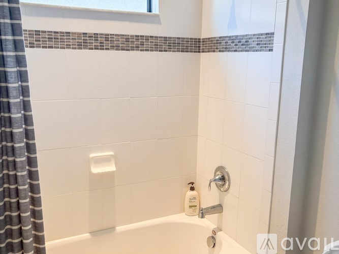 A white bathtub with a shower curtain and a bottle of soap on the side.