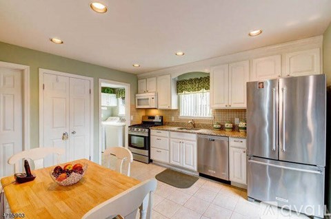 A kitchen with white cabinets and a wooden table with a bowl of fruit on it.