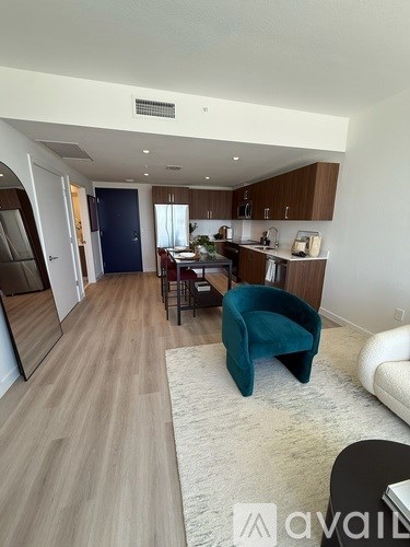A living room with a teal chair and a kitchen area in the background.