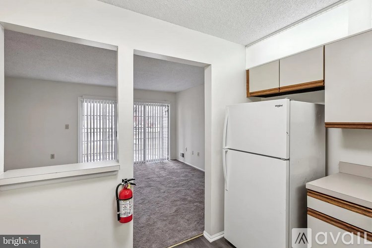 A bright, empty room with a white refrigerator and a fire extinguisher on the wall.