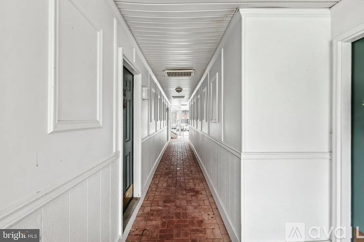 A long hallway with white walls and a red tile floor.