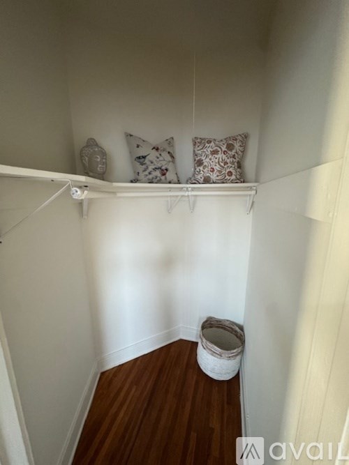 A small room with a wooden floor and a white wall with a shelf and two pillows.