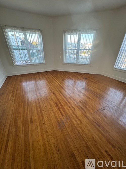 A room with wooden flooring and two windows.