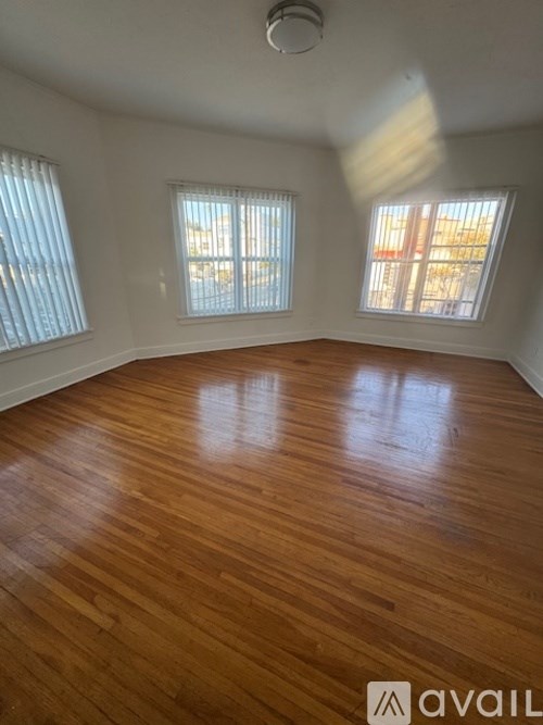 A room with wooden flooring and two windows.