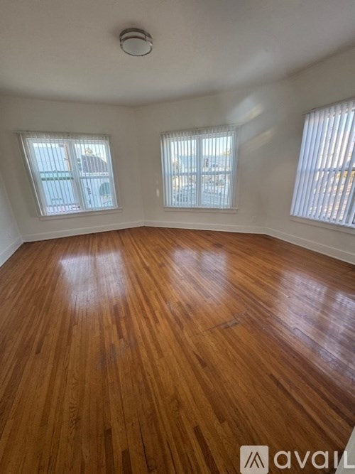 A room with wooden flooring and three windows.