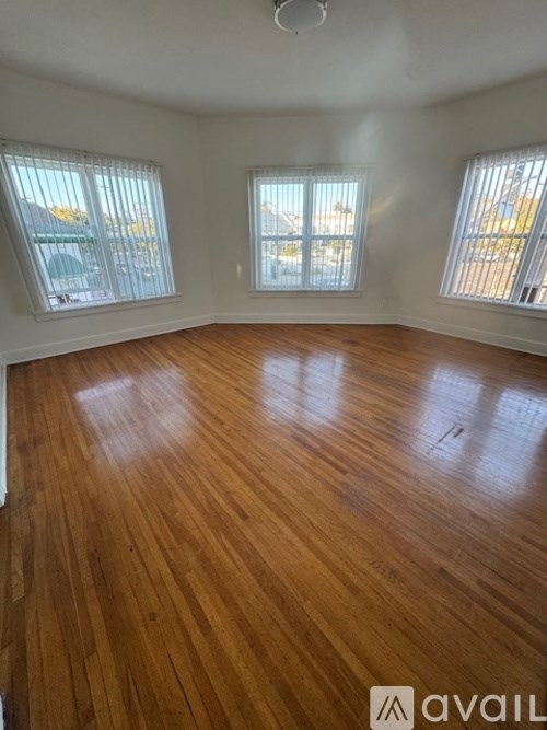 A room with wooden flooring and two windows.