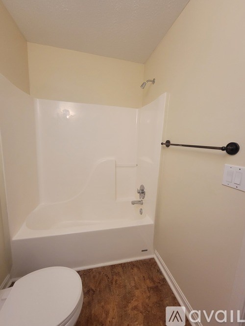 A white toilet sits in a bathroom with a white tub and a wooden floor.