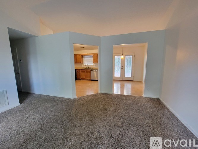 A carpeted room with a kitchen visible through a doorway.