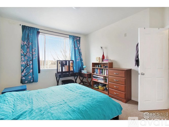 A bedroom with a blue bedspread and a window with blue curtains.