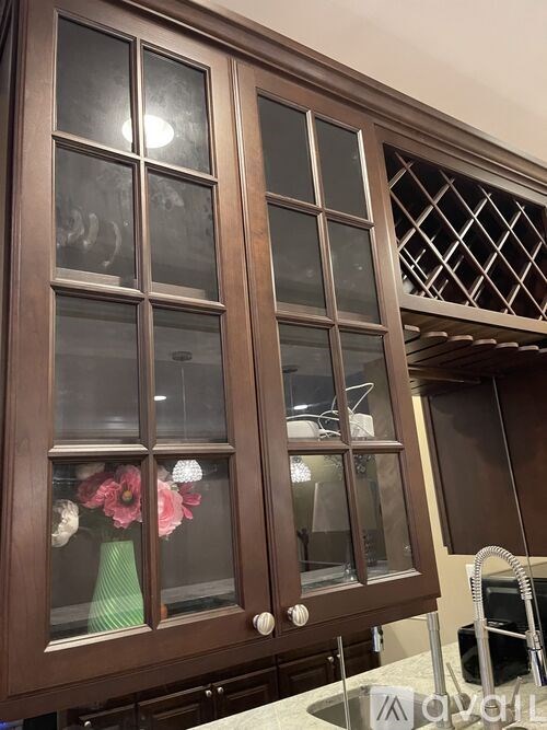 Brown cabinet with glass doors and a vase of flowers inside.