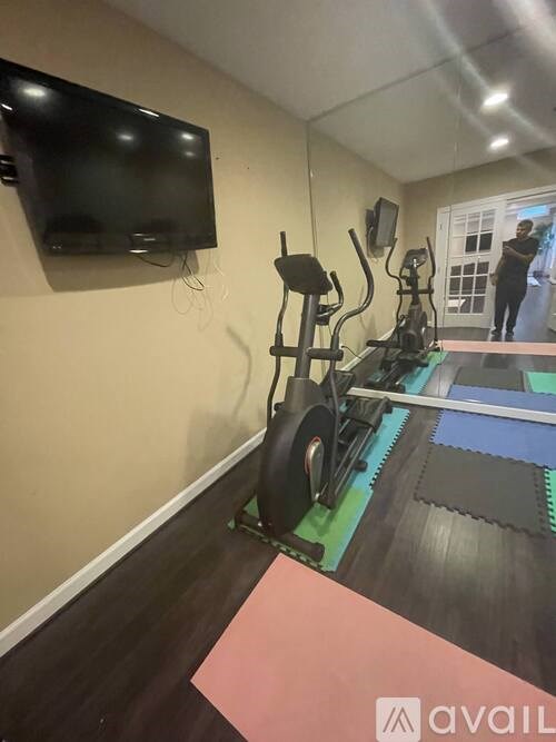 A gym room with a rowing machine and a television mounted on the wall.