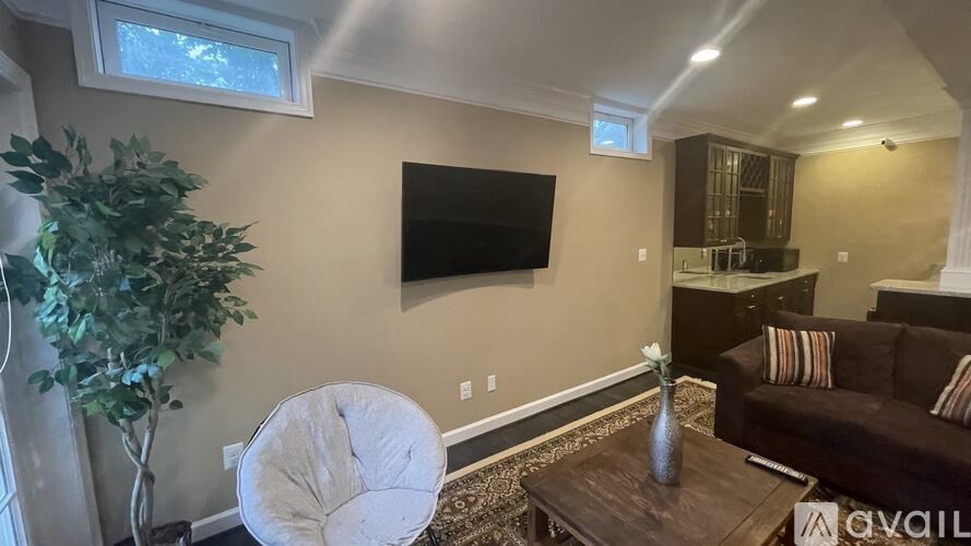 A living room with a white chair, a brown couch, and a flat screen TV mounted on the wall.