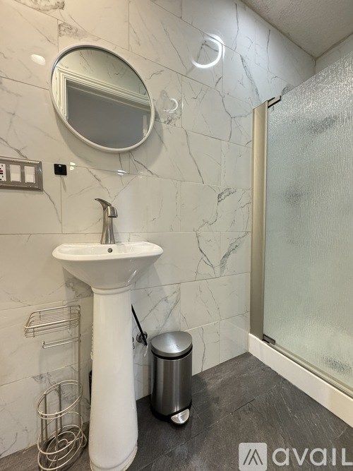 A bathroom with a white pedestal sink and a round mirror.