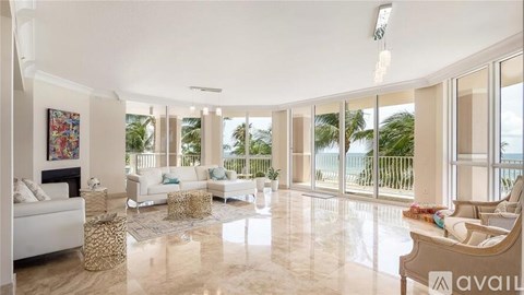 A spacious living room with white furniture and a view of the outdoors through large windows.