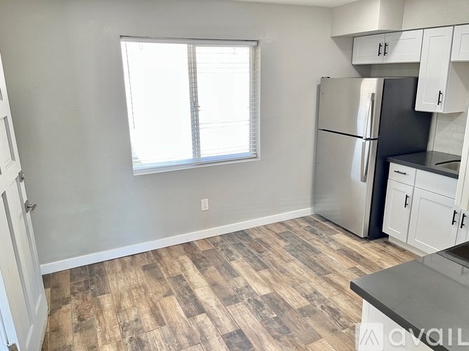 A kitchen with a refrigerator, cabinets, and a wooden floor.