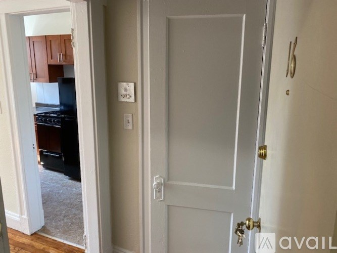 A white door with a gold handle is in a room with a white wall and a switch.