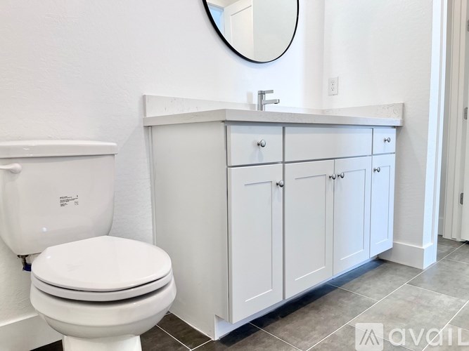A white toilet sits next to a white cabinet with a round mirror above it.