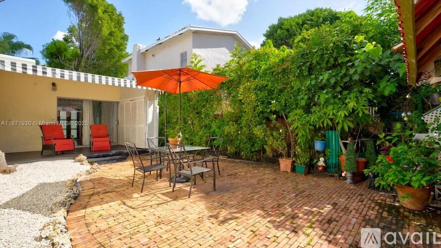 A patio with a table and chairs is surrounded by greenery.