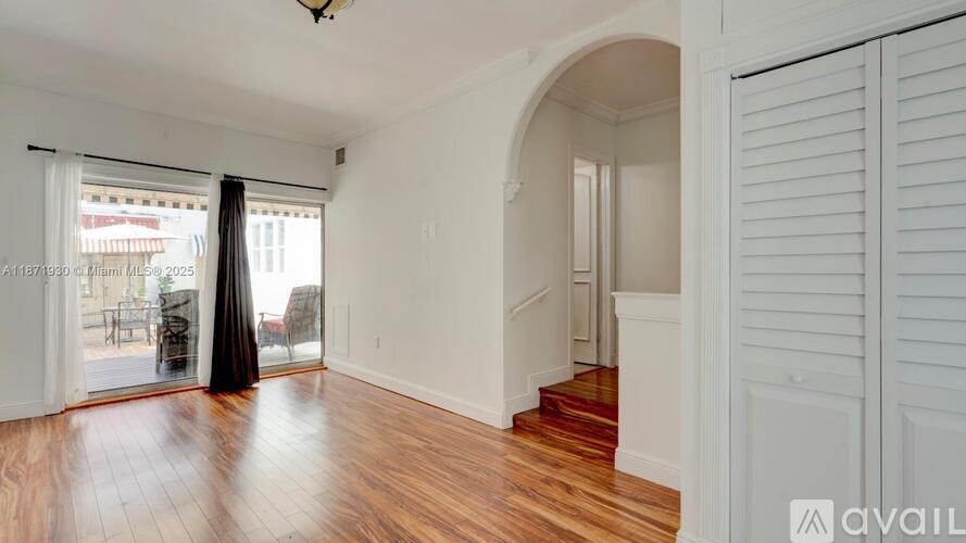 A room with wooden floors and white walls, with a staircase leading to another room.
