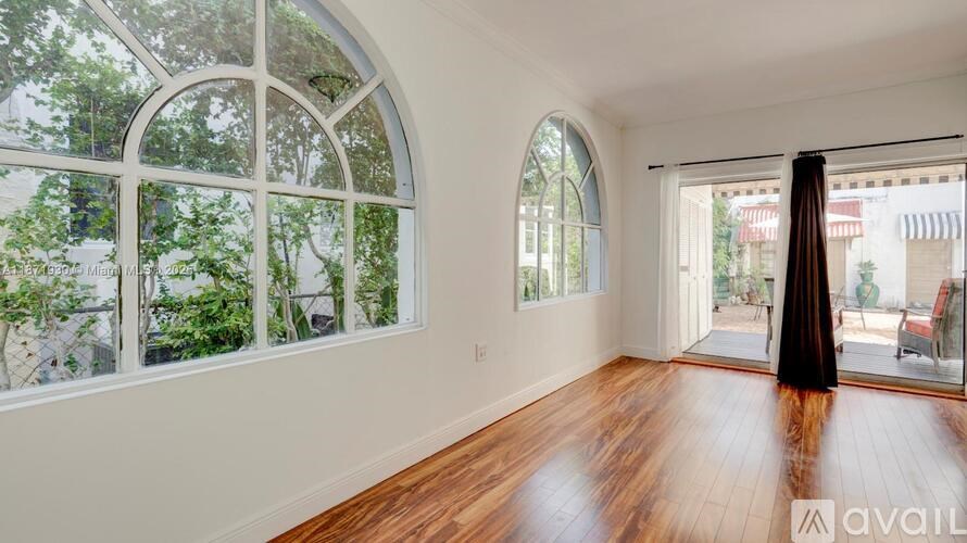 A room with wooden floors and large windows with a view of trees and buildings outside.