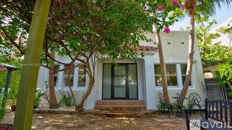 A house with a white exterior and a glass door is surrounded by greenery.