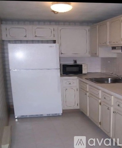A white refrigerator is in a kitchen with white cabinets.