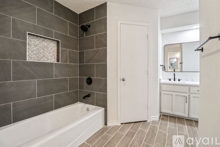 A bathroom with a white tub and grey tiles.