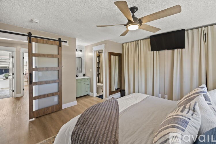 A bedroom with a bed, a ceiling fan, and a sliding door leading to a balcony.