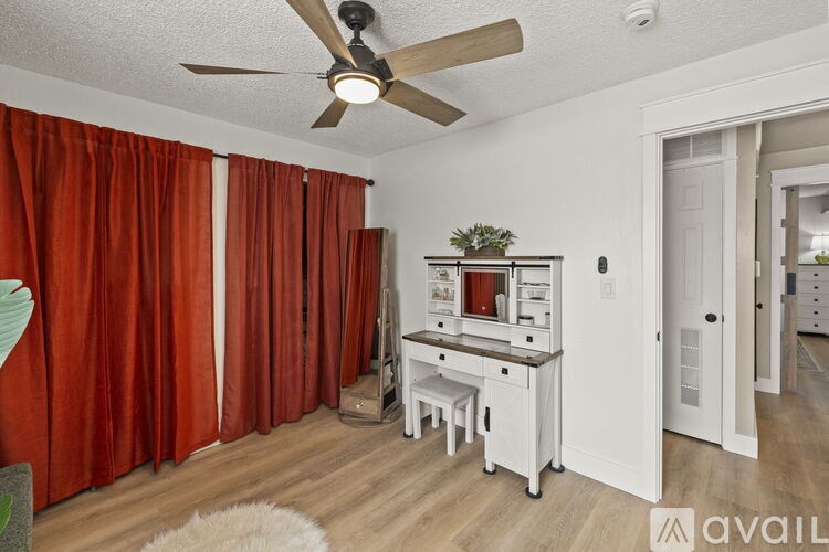 A room with a fan, a table with a plant on it, and a white door.