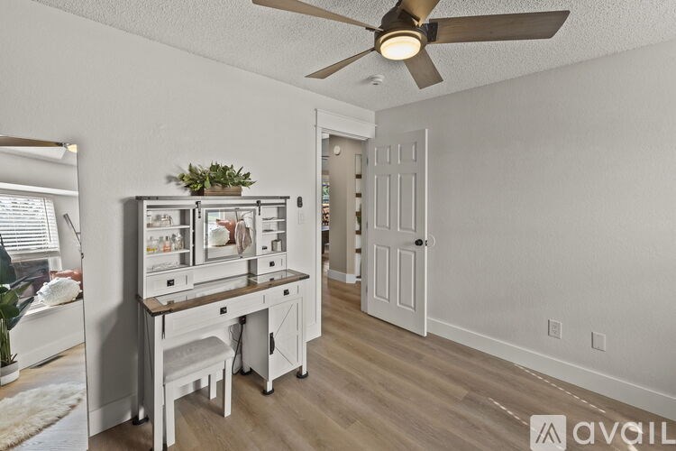 A room with a white table and chairs, a ceiling fan, and a door leading to another room.