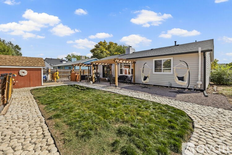 A house with a grey exterior and a white window is surrounded by a grassy area and a stone pathway.