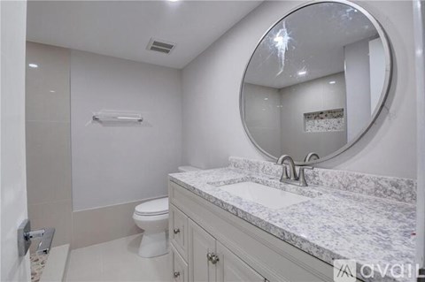 A white bathroom with a marble counter top and a round mirror.