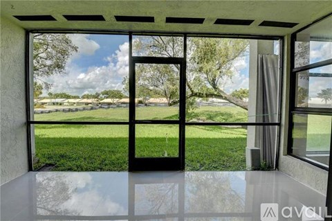 A room with a view of a green lawn and trees through the windows.