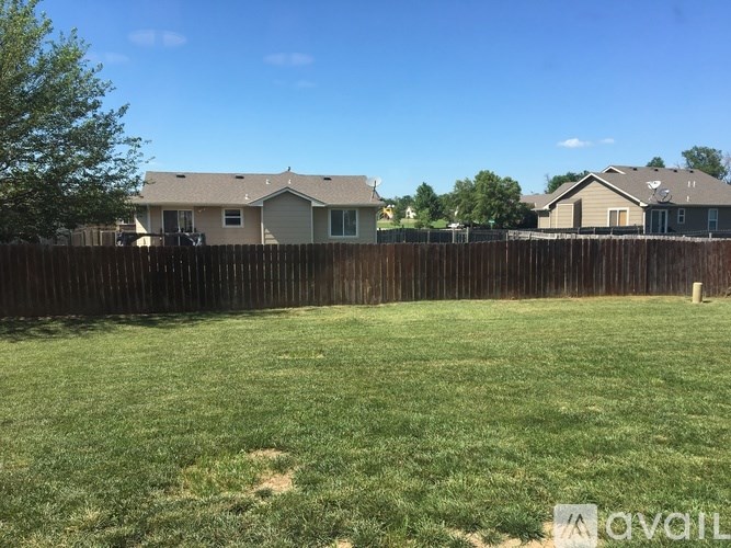 A grassy field with a wooden fence and houses in the background.