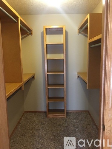 A tall wooden shelf unit with multiple shelves is in a room with carpeted flooring.