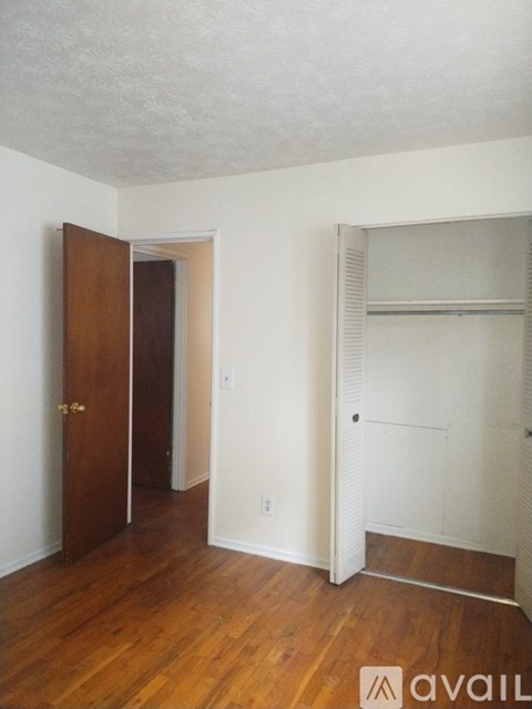 A room with a wooden floor and a white wall with a door and a shelf.