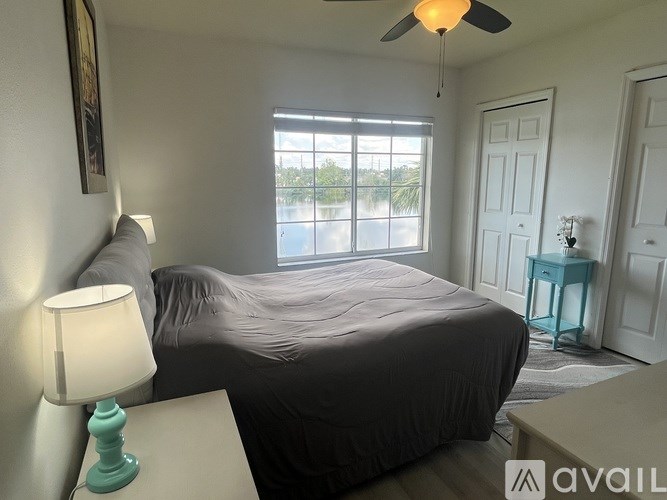 A bedroom with a bed, a nightstand with a lamp, and a ceiling fan.