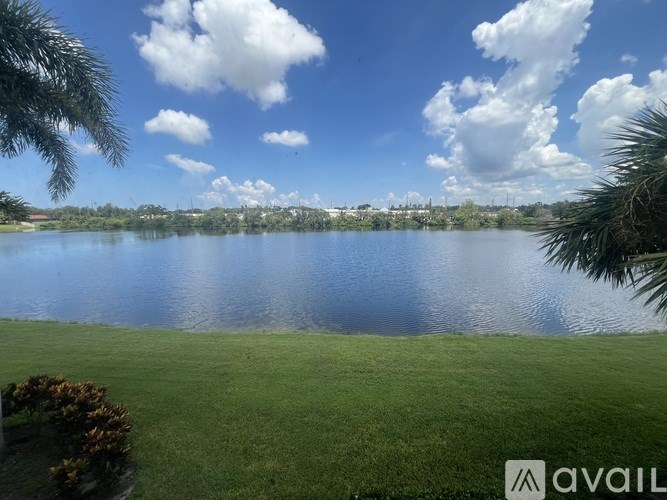 A large body of water surrounded by green grass and trees under a blue sky with clouds.