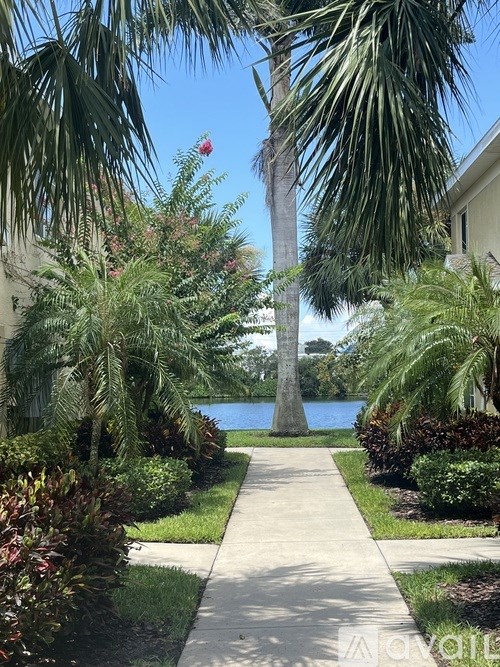 A pathway leads to a house with a palm tree and a lake in the background.