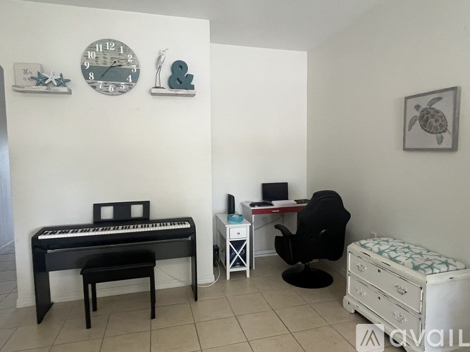 A room with a piano, a desk with a chair, and a bed.