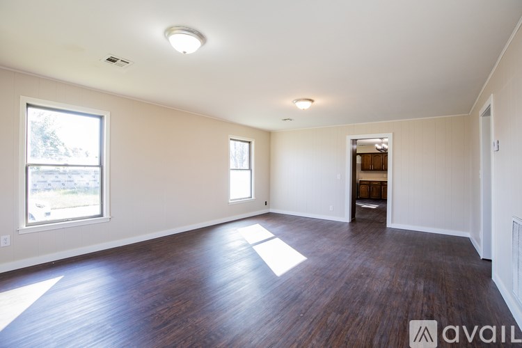 A spacious room with wooden floors and two windows.