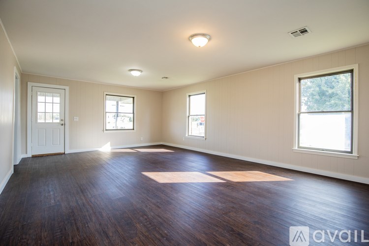 A spacious room with wooden floors and three windows.