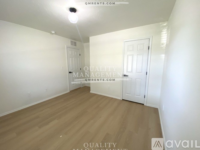 A room with wooden flooring and two white doors, one of which is closed.