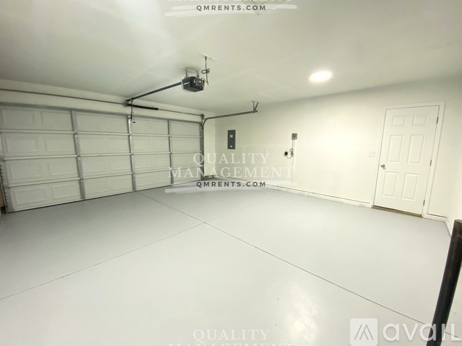 A spacious garage with a white floor and a closed white door on the right side.