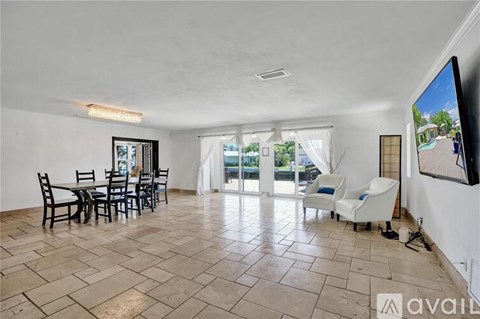 A living room with a television, a dining table and chairs, and a sliding glass door leading to a balcony.