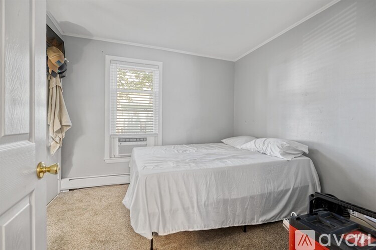 A bedroom with a bed, a window with blinds, and a suitcase.